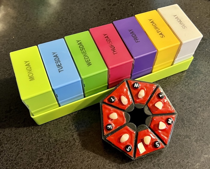 Photo of a colorful pill organizer set with one box for every day of the week and a daily organizer from Pill Joy that's decorated with red resin and individual fake teeth on top of every compartment.